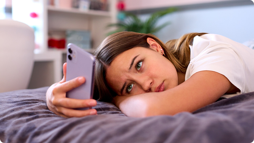 Adolescente aux traits tristes et inquiets seule dans sa chambre regardant son téléphone cellulaire.